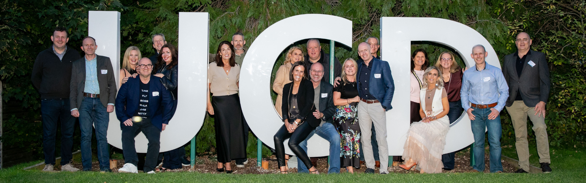 UCD alumni posing by the giant UCD letters by the main UCD lake, back on campus for their class reunion.